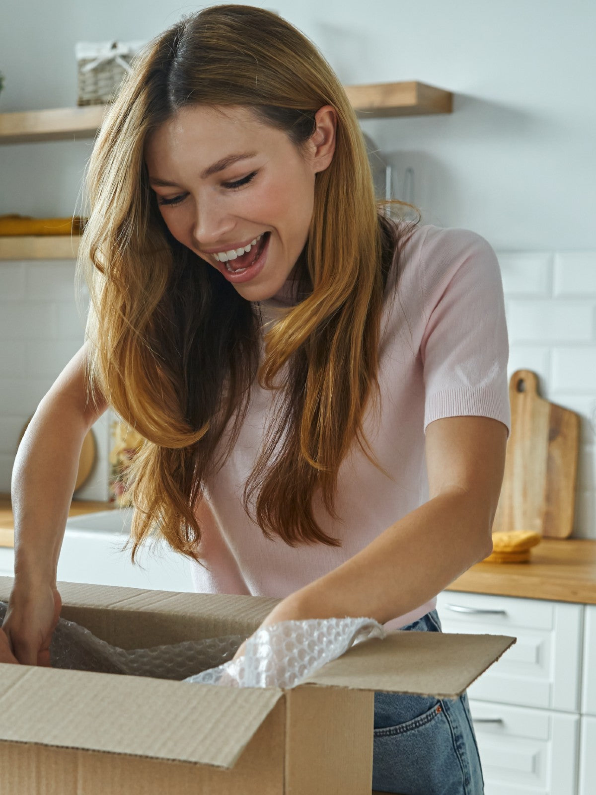 Frau packt in einer hellen Küche lachend ein Paket aus